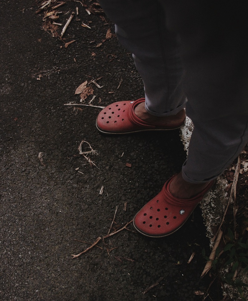 picture of a person wearing red clogs and black trousers, standing on a concrete 