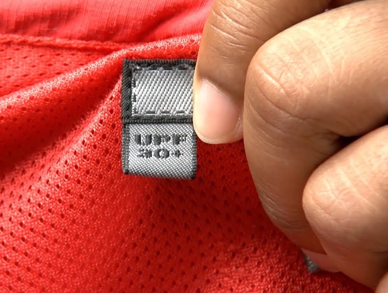  A close-up image of a hand holding a red fabric tag on golf wear that reads "UPF 30+," indicating sun protection.